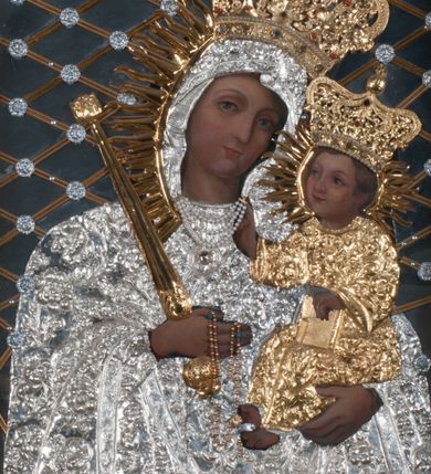 Zdjęcie nr 1: Obraz w kształcie prostokąta zamkniętego łukiem półpełnym, ujęty w profilowaną, złoconą ramą zdobioną kimationem. Tło niebiesko-szare, ze złotą, regencyjną kratą dekorowaną srebrnymi rozetami na przecięciach listew. Matka Boska ukazana w półpostaci, z głową zwróconą en trois quarts w lewo, prawą ręką uniesioną na wysokość piersi, podtrzymuje złote, tralkowate berło, lewą unosi Dzieciątko. Twarz owalna o beżowobrązowej karnacji, z prostym nosem, jasnoczerwonymi, uśmięchniętymi ustami, brązowymi oczami i regularnymi łukami brwiowymi. Głowa ujęta promienistą glorią. Chrystus siedzący na ramieniu matki, lewą ręką podtrzymuje zamkniętą księgę, prawą unosi na wysokość piersi w geście błogosławieństwa. Twarz, okrągła, o brązowobeżowej karnacji, z prostym nosem, lekko uśmiechniętymi ustami, brązowymi oczami, okolona krótkimi, prostymi włosami. Twarze i dłonie obu postaci odsłonięte, reszta przesłonięta srebrną sukienką z ornamentem roślinnym. Na głowie Matki Boskiej i Dzieciątka złocone, zamknięte, kameryzowane korony, zwieńczone krzyżami na kulach.