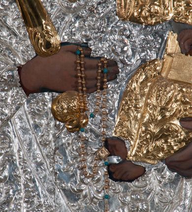 Zdjęcie nr 7: Obraz w kształcie prostokąta zamkniętego łukiem półpełnym, ujęty w profilowaną, złoconą ramą zdobioną kimationem. Tło niebiesko-szare, ze złotą, regencyjną kratą dekorowaną srebrnymi rozetami na przecięciach listew. Matka Boska ukazana w półpostaci, z głową zwróconą en trois quarts w lewo, prawą ręką uniesioną na wysokość piersi, podtrzymuje złote, tralkowate berło, lewą unosi Dzieciątko. Twarz owalna o beżowobrązowej karnacji, z prostym nosem, jasnoczerwonymi, uśmięchniętymi ustami, brązowymi oczami i regularnymi łukami brwiowymi. Głowa ujęta promienistą glorią. Chrystus siedzący na ramieniu matki, lewą ręką podtrzymuje zamkniętą księgę, prawą unosi na wysokość piersi w geście błogosławieństwa. Twarz, okrągła, o brązowobeżowej karnacji, z prostym nosem, lekko uśmiechniętymi ustami, brązowymi oczami, okolona krótkimi, prostymi włosami. Twarze i dłonie obu postaci odsłonięte, reszta przesłonięta srebrną sukienką z ornamentem roślinnym. Na głowie Matki Boskiej i Dzieciątka złocone, zamknięte, kameryzowane korony, zwieńczone krzyżami na kulach.