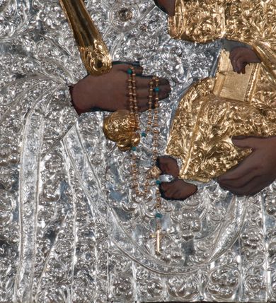 Zdjęcie nr 5: Obraz w kształcie prostokąta zamkniętego łukiem półpełnym, ujęty w profilowaną, złoconą ramą zdobioną kimationem. Tło niebiesko-szare, ze złotą, regencyjną kratą dekorowaną srebrnymi rozetami na przecięciach listew. Matka Boska ukazana w półpostaci, z głową zwróconą en trois quarts w lewo, prawą ręką uniesioną na wysokość piersi, podtrzymuje złote, tralkowate berło, lewą unosi Dzieciątko. Twarz owalna o beżowobrązowej karnacji, z prostym nosem, jasnoczerwonymi, uśmięchniętymi ustami, brązowymi oczami i regularnymi łukami brwiowymi. Głowa ujęta promienistą glorią. Chrystus siedzący na ramieniu matki, lewą ręką podtrzymuje zamkniętą księgę, prawą unosi na wysokość piersi w geście błogosławieństwa. Twarz, okrągła, o brązowobeżowej karnacji, z prostym nosem, lekko uśmiechniętymi ustami, brązowymi oczami, okolona krótkimi, prostymi włosami. Twarze i dłonie obu postaci odsłonięte, reszta przesłonięta srebrną sukienką z ornamentem roślinnym. Na głowie Matki Boskiej i Dzieciątka złocone, zamknięte, kameryzowane korony, zwieńczone krzyżami na kulach.