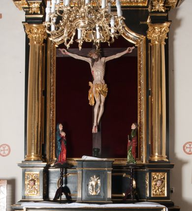 Zdjęcie nr 1: Nastawa ołtarzowa architektoniczna, jednokondygnacyjna, jednoosiowa. Pośrodku prostokątna nisza zwieńczona łukiem wklęsło-wypukłym ściętym, w bogato profilowanej, rzeźbionej i złoconej ramie zdobionej motywami roślinnymi. Nisza flankowana kolumnami o kompozytowych kapitelach, umieszczonymi na wysokich postumentach i na tle par wąskich prostokątnych płycin. Kolumny podtrzymują odcinki uproszczonego belkowania i gzyms, występujące nad podporami. Ponad gzymsem, w osiach kolumn odcinki przerwanego przyczółka. Predella zdobiona płyciną o kształcie prostokąta leżącego, z krótszymi bokami zamkniętymi łukiem nadwieszonym. We fryzie ponad kolumnami rozetki. Gzyms i naczółek zdobione akantem, rama rozetami i ornamentem roślinnym, konsole akantem i główkami puttów. Nisza ołtarza wtórnie wyłożona czerwonym aksamitem. W niej rzeźba Chrystus Ukrzyżowany. Mensa prostopadłościenna, z antepedium ujętym profilowaną ramą i zdobionym ukośną kratką, z motywami Arma Christi pośrodku oraz ażurowymi, złoconymi motywami liści w narożach. Ściany boczne ozdobione prostokątnymi płycinami. Na mensie tabernakulum drewniane, prostopadłościenne, jednoosiowe, jednokondygnacyjne. Ściana frontowa flankowana kanelowanymi pilastrami, wspierającymi uproszczone belkowanie. Pomiędzy nimi prostokątne, jednoskrzydłowe drzwiczki, ozdobione motywem złotego kielicha ze srebrną hostią, kłosami zbóż i winoroślą.  Po bokach tabernakulum rzeźby asystencyjne Matka Boska Bolesna i Św. Jan Ewangelista, ustawione na wysokich stojakach