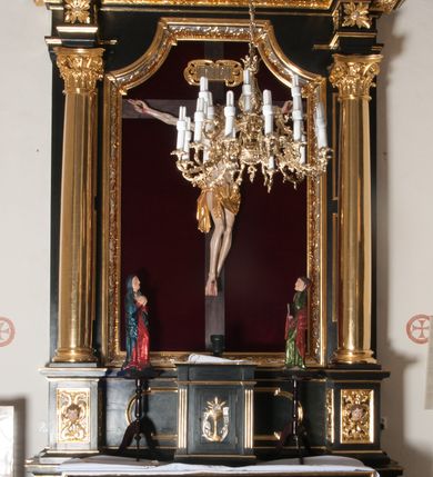 Zdjęcie nr 2: Nastawa ołtarzowa architektoniczna, jednokondygnacyjna, jednoosiowa. Pośrodku prostokątna nisza zwieńczona łukiem wklęsło-wypukłym ściętym, w bogato profilowanej, rzeźbionej i złoconej ramie zdobionej motywami roślinnymi. Nisza flankowana kolumnami o kompozytowych kapitelach, umieszczonymi na wysokich postumentach i na tle par wąskich prostokątnych płycin. Kolumny podtrzymują odcinki uproszczonego belkowania i gzyms, występujące nad podporami. Ponad gzymsem, w osiach kolumn odcinki przerwanego przyczółka. Predella zdobiona płyciną o kształcie prostokąta leżącego, z krótszymi bokami zamkniętymi łukiem nadwieszonym. We fryzie ponad kolumnami rozetki. Gzyms i naczółek zdobione akantem, rama rozetami i ornamentem roślinnym, konsole akantem i główkami puttów. Nisza ołtarza wtórnie wyłożona czerwonym aksamitem. W niej rzeźba Chrystus Ukrzyżowany. Mensa prostopadłościenna, z antepedium ujętym profilowaną ramą i zdobionym ukośną kratką, z motywami Arma Christi pośrodku oraz ażurowymi, złoconymi motywami liści w narożach. Ściany boczne ozdobione prostokątnymi płycinami. Na mensie tabernakulum drewniane, prostopadłościenne, jednoosiowe, jednokondygnacyjne. Ściana frontowa flankowana kanelowanymi pilastrami, wspierającymi uproszczone belkowanie. Pomiędzy nimi prostokątne, jednoskrzydłowe drzwiczki, ozdobione motywem złotego kielicha ze srebrną hostią, kłosami zbóż i winoroślą.  Po bokach tabernakulum rzeźby asystencyjne Matka Boska Bolesna i Św. Jan Ewangelista, ustawione na wysokich stojakach