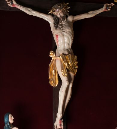 Zdjęcie nr 2: Chrystus, w typie Christo morto, rozpięty na drewnianym, prostym krzyżu łacińskim z titulusem z napisem INRI ujętym małżowiną. Chrystus przybity trzema gwoździami, w lekkim zwisie ciała i nogami ugiętymi w kolanach, ze stopami założonymi prawa na lewą. Na biodrach złocone, pofałdowane perizonium przytrzymywany sznurem; prawe biodro odsłonięte. Ciało smukłe, szczupłe, z wyraźnie zaznaczoną muskulaturą, ścięgnami i żebrami. Karnacja jasna ze strużkami krwi wypływającymi z ran. Głowa w koronie cierniowej, opuszczona i przechylona na prawy bark. Oczy zamknięte. Włosy brązowe, długie, kręcone, broda o rozdwojonych końcach. Na głowie korona cierniowa.