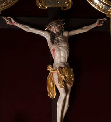 Zdjęcie nr 1: Chrystus, w typie Christo morto, rozpięty na drewnianym, prostym krzyżu łacińskim z titulusem z napisem INRI ujętym małżowiną. Chrystus przybity trzema gwoździami, w lekkim zwisie ciała i nogami ugiętymi w kolanach, ze stopami założonymi prawa na lewą. Na biodrach złocone, pofałdowane perizonium przytrzymywany sznurem; prawe biodro odsłonięte. Ciało smukłe, szczupłe, z wyraźnie zaznaczoną muskulaturą, ścięgnami i żebrami. Karnacja jasna ze strużkami krwi wypływającymi z ran. Głowa w koronie cierniowej, opuszczona i przechylona na prawy bark. Oczy zamknięte. Włosy brązowe, długie, kręcone, broda o rozdwojonych końcach. Na głowie korona cierniowa.