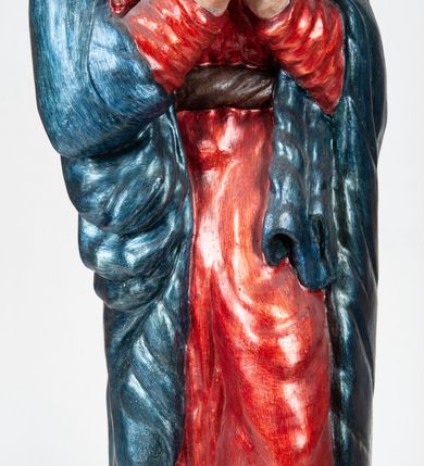 Zdjęcie nr 6: Rzeźba pełnoplastyczna, ukazująca Matkę Boską Bolesną w całej postaci. Matka Boska stoi w lekkim kontrapoście, ciężar ciała wspierając na prawej nodze, z dłońmi splecionymi na wysokości piersi w modlitewnym geście, z głową lekko odchyloną do tyłu i wzrokiem skierowanym ku górze. Twarz potraktowana schematycznie. Maria ubrana w czerwoną suknię przepasaną brązowym sznurem i niebieski płaszcz założony na głowę i barki, podtrzymywany z przodu przedramionami. Wokół szyi biała chusta.