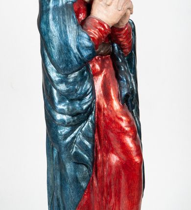 Zdjęcie nr 4: Rzeźba pełnoplastyczna, ukazująca Matkę Boską Bolesną w całej postaci. Matka Boska stoi w lekkim kontrapoście, ciężar ciała wspierając na prawej nodze, z dłońmi splecionymi na wysokości piersi w modlitewnym geście, z głową lekko odchyloną do tyłu i wzrokiem skierowanym ku górze. Twarz potraktowana schematycznie. Maria ubrana w czerwoną suknię przepasaną brązowym sznurem i niebieski płaszcz założony na głowę i barki, podtrzymywany z przodu przedramionami. Wokół szyi biała chusta.