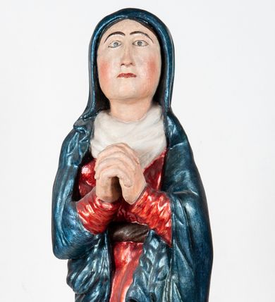 Zdjęcie nr 1: Rzeźba pełnoplastyczna, ukazująca Matkę Boską Bolesną w całej postaci. Matka Boska stoi w lekkim kontrapoście, ciężar ciała wspierając na prawej nodze, z dłońmi splecionymi na wysokości piersi w modlitewnym geście, z głową lekko odchyloną do tyłu i wzrokiem skierowanym ku górze. Twarz potraktowana schematycznie. Maria ubrana w czerwoną suknię przepasaną brązowym sznurem i niebieski płaszcz założony na głowę i barki, podtrzymywany z przodu przedramionami. Wokół szyi biała chusta.