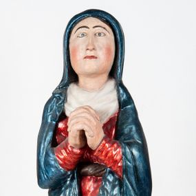 Zdjęcie nr 1: Rzeźba pełnoplastyczna, ukazująca Matkę Boską Bolesną w całej postaci. Matka Boska stoi w lekkim kontrapoście, ciężar ciała wspierając na prawej nodze, z dłońmi splecionymi na wysokości piersi w modlitewnym geście, z głową lekko odchyloną do tyłu i wzrokiem skierowanym ku górze. Twarz potraktowana schematycznie. Maria ubrana w czerwoną suknię przepasaną brązowym sznurem i niebieski płaszcz założony na głowę i barki, podtrzymywany z przodu przedramionami. Wokół szyi biała chusta.