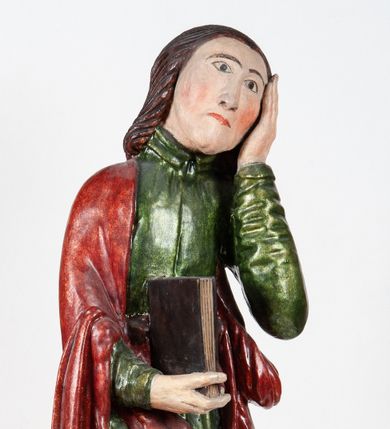 Zdjęcie nr 1: Rzeźba pełnoplastyczna, przedstawiająca św. Jana Ewangelistę w całej postaci. Apostoł stoi w lekkim kontrapoście, ciężar ciała wspierając na lewej nodze, z głową przechyloną na lewy bark. Prawą dłonią, uniesioną na wysokość pasa, podtrzymuje zamkniętą księgę, lewą dłoń przyciska do policzka w geście bólu i rozpaczy. Twarz potraktowana schematycznie, okolona długimi, brązowymi włosami z przedziałkiem pośrodku głowy. Święty ubrany w zieloną, długa tunikę, przewiązaną w pasie sznurem oraz czerwony płaszcz zarzucony na prawy bark i okrywający plecy, z przodu podtrzymywany prawym przedramieniem. Stopy bose.