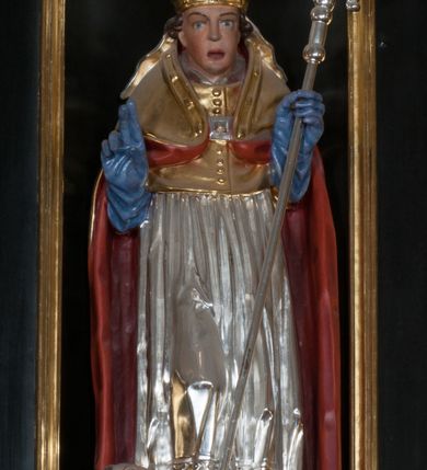 Zdjęcie nr 2: Rzeźba pełnoplastyczna, przeznaczona do umieszczenia w niszy, przedstawienie świętego w całej postaci umieszczone na niskim postumencie. Św. Stanisław ukazany jest frontalnie, w pozycji stojącej, w kontrapoście, z głową lekko pochyloną do przodu. Ręce ugięte w łokciach - w lewej pastorał, prawą wykonuje gest błogosławieństwa. Twarz pociągła, łukowato wygięte brwi, oczy szeroko otwarte, nos prosty, usta lekko rozchylone. Na głowie srebrno-złota infuła, spod której widoczne pukle kręconych włosów. Święty odziany jest w złotą kapę z czerwoną podszewką, spiętą na piersi fibulą, złoty mucet, rokietę, złotą albę, błękitne rękawiczki i brązowe buty. Rokieta fałdowana głęboko ciętymi, cienkimi, pionowymi fałdami, z jedną łukowato wygiętą fałdą. Alba z fałdami na kształt cienkich rurek, załamujących się u podstawy. Przy podstawie niewielka postać powstającego z grobu Piotrowina. Mężczyzna ukazany w trzech czwartych, zwrócony w lewo, z głową uniesioną w stronę świętego, prawą ręką na piersi, lewą wyprostowaną. Nogi ugięte w kolanach. Twarz pociągłą z wąsami. Włosy brązowe, krótkie, kręcone. Przepasany białą tkaniną, z ukośnymi, głęboko ciętymi fałdami.