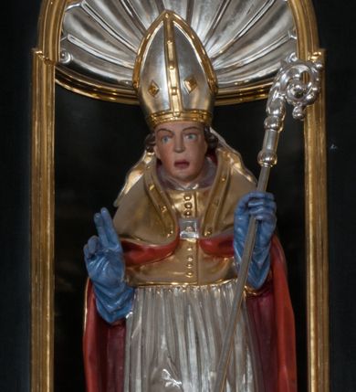 Zdjęcie nr 1: Rzeźba pełnoplastyczna, przeznaczona do umieszczenia w niszy, przedstawienie świętego w całej postaci umieszczone na niskim postumencie. Św. Stanisław ukazany jest frontalnie, w pozycji stojącej, w kontrapoście, z głową lekko pochyloną do przodu. Ręce ugięte w łokciach - w lewej pastorał, prawą wykonuje gest błogosławieństwa. Twarz pociągła, łukowato wygięte brwi, oczy szeroko otwarte, nos prosty, usta lekko rozchylone. Na głowie srebrno-złota infuła, spod której widoczne pukle kręconych włosów. Święty odziany jest w złotą kapę z czerwoną podszewką, spiętą na piersi fibulą, złoty mucet, rokietę, złotą albę, błękitne rękawiczki i brązowe buty. Rokieta fałdowana głęboko ciętymi, cienkimi, pionowymi fałdami, z jedną łukowato wygiętą fałdą. Alba z fałdami na kształt cienkich rurek, załamujących się u podstawy. Przy podstawie niewielka postać powstającego z grobu Piotrowina. Mężczyzna ukazany w trzech czwartych, zwrócony w lewo, z głową uniesioną w stronę świętego, prawą ręką na piersi, lewą wyprostowaną. Nogi ugięte w kolanach. Twarz pociągłą z wąsami. Włosy brązowe, krótkie, kręcone. Przepasany białą tkaniną, z ukośnymi, głęboko ciętymi fałdami.