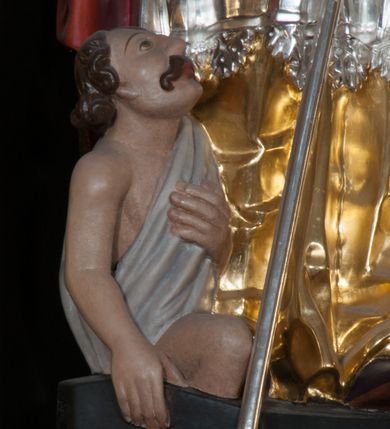 Zdjęcie nr 4: Rzeźba pełnoplastyczna, przeznaczona do umieszczenia w niszy, przedstawienie świętego w całej postaci umieszczone na niskim postumencie. Św. Stanisław ukazany jest frontalnie, w pozycji stojącej, w kontrapoście, z głową lekko pochyloną do przodu. Ręce ugięte w łokciach - w lewej pastorał, prawą wykonuje gest błogosławieństwa. Twarz pociągła, łukowato wygięte brwi, oczy szeroko otwarte, nos prosty, usta lekko rozchylone. Na głowie srebrno-złota infuła, spod której widoczne pukle kręconych włosów. Święty odziany jest w złotą kapę z czerwoną podszewką, spiętą na piersi fibulą, złoty mucet, rokietę, złotą albę, błękitne rękawiczki i brązowe buty. Rokieta fałdowana głęboko ciętymi, cienkimi, pionowymi fałdami, z jedną łukowato wygiętą fałdą. Alba z fałdami na kształt cienkich rurek, załamujących się u podstawy. Przy podstawie niewielka postać powstającego z grobu Piotrowina. Mężczyzna ukazany w trzech czwartych, zwrócony w lewo, z głową uniesioną w stronę świętego, prawą ręką na piersi, lewą wyprostowaną. Nogi ugięte w kolanach. Twarz pociągłą z wąsami. Włosy brązowe, krótkie, kręcone. Przepasany białą tkaniną, z ukośnymi, głęboko ciętymi fałdami.