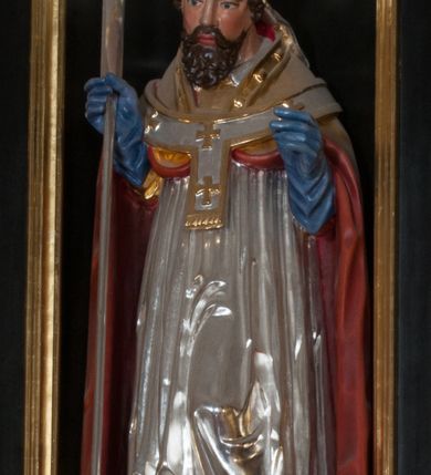 Zdjęcie nr 3: Rzeźba pełnoplastyczna, przyścienna, przeznaczona do umieszczenia w niszy, przedstawiająca św. Wojciecha w całej postaci, na niskim postumencie. Święty ukazany frontalnie, w pozycji stojącej, w kontrapoście, z głową lekko pochyloną. Ręce ugięte w łokciach, prawą dłonią trzyma wiosło. Pociągłą twarz okala ciemna, falowana broda i wąsy. Brwi cienkie, nos prosty. Na głowie srebrno-złota infuła, spod której widoczne pukle kręconych włosów. Święty odziany jest w złotą kapę z czerwoną podszewką, biały paliusz ze złotymi krzyżami, rokietę, złotą albę, błękitne rękawiczki i brązowe buty. Rokieta fałdowana głęboko ciętymi, cienkimi, pionowymi fałdami, z jedną łukowato wygiętą fałdą. Alba z fałdami na kształt cienkich rurek, załamujących się u podstawy.