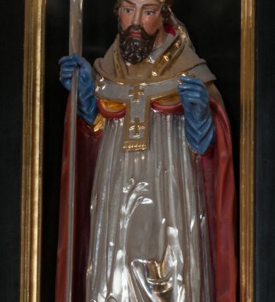 Zdjęcie nr 8: Rzeźba pełnoplastyczna, przyścienna, przeznaczona do umieszczenia w niszy, przedstawiająca św. Wojciecha w całej postaci, na niskim postumencie. Święty ukazany frontalnie, w pozycji stojącej, w kontrapoście, z głową lekko pochyloną. Ręce ugięte w łokciach, prawą dłonią trzyma wiosło. Pociągłą twarz okala ciemna, falowana broda i wąsy. Brwi cienkie, nos prosty. Na głowie srebrno-złota infuła, spod której widoczne pukle kręconych włosów. Święty odziany jest w złotą kapę z czerwoną podszewką, biały paliusz ze złotymi krzyżami, rokietę, złotą albę, błękitne rękawiczki i brązowe buty. Rokieta fałdowana głęboko ciętymi, cienkimi, pionowymi fałdami, z jedną łukowato wygiętą fałdą. Alba z fałdami na kształt cienkich rurek, załamujących się u podstawy.