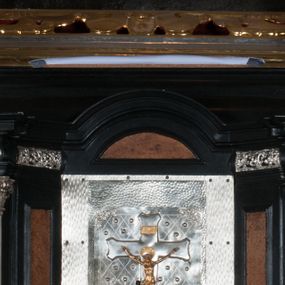 Zdjęcie nr 1: Tabernakulum na rzucie połowy ośmioboku, architektoniczne, na niskim postumencie, trójosiowe, dwudzielne (z wydzieloną gzymsem częścią cokołową), artykułowane kolumienkami o kapitelach kompozytowych oraz wolutami podtrzymującymi kompozytowe kapitele, na wybrzuszonych, zdwojonych cokołach. Belkowanie występujące nad podporami. Ścianka z drzwiczkami zamknięta łukiem półkolistym. Cokoliki, fryz i boczne ścianki tabernakulum zdobione suchym akantem. Drzwiczki jednoskrzydłowe (nowsze, pierwotne dwuskrzydłowe), srebrne, zdobione prostokątną płyciną, z romboidalnymi polami i spłaszczonymi kulami. W narożach stylizowany ornament roślinny. W centrum przedstawienie Chrystusa na krzyżu. Pola bocznych ścianek zdobione imitującymi szufladki mozaikowymi płycinami z różnobarwnych marmurów przedstawiającymi pejzaż z elementami architektury oraz płycinami wykładanymi jasnym drewnem. Pejzażowe płyciny w górnej części tabernakulum ujęte srebrnymi, odlewanymi i cyzelowanym ramkami. 
Na tabernakulum umieszczone antytetycznie rzeźby dwóch aniołów: pełnoplastyczne, w ujęciu całopostaciowym, wolnostojące. Anioł po lewej stronie ukazany jest w pozycji klęczącej, z profilu, pochylony do przodu. W rękach trzyma łódkę na kadzidło. Włosy brązowe, falowane, sięgające do ramion. Twarz pociągła, łukowato wygięte brwi, szeroko otwarte oczy, prosty nos, róż na policzkach. Skrzydła złote. Anioł odziany jest białą tunikę, z krótkimi rękawami i z cienkimi, pionowymi fałdami, załamującymi się na wysokości kolan. Stopy bose. Anioł po prawej ukazany jest w pozycji klęczącej, z profilu, pochylony do przodu. W rękach trzyma trybularz. Włosy brązowe, falowane, sięgające do ramion. Twarz pociągła, łukowato wygięte brwi, szeroko otwarte oczy, prosty nos, róż na policzkach. Skrzydła złote. Anioł odziany jest białą tunikę, z krótkimi rękawami i z cienkimi, pionowymi fałdami, załamującymi się na wysokości kolan. Stopy bose.
