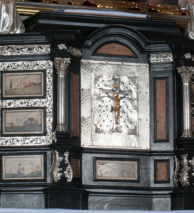 Zdjęcie nr 4: Tabernakulum na rzucie połowy ośmioboku, architektoniczne, na niskim postumencie, trójosiowe, dwudzielne (z wydzieloną gzymsem częścią cokołową), artykułowane kolumienkami o kapitelach kompozytowych oraz wolutami podtrzymującymi kompozytowe kapitele, na wybrzuszonych, zdwojonych cokołach. Belkowanie występujące nad podporami. Ścianka z drzwiczkami zamknięta łukiem półkolistym. Cokoliki, fryz i boczne ścianki tabernakulum zdobione suchym akantem. Drzwiczki jednoskrzydłowe (nowsze, pierwotne dwuskrzydłowe), srebrne, zdobione prostokątną płyciną, z romboidalnymi polami i spłaszczonymi kulami. W narożach stylizowany ornament roślinny. W centrum przedstawienie Chrystusa na krzyżu. Pola bocznych ścianek zdobione imitującymi szufladki mozaikowymi płycinami z różnobarwnych marmurów przedstawiającymi pejzaż z elementami architektury oraz płycinami wykładanymi jasnym drewnem. Pejzażowe płyciny w górnej części tabernakulum ujęte srebrnymi, odlewanymi i cyzelowanym ramkami. 
Na tabernakulum umieszczone antytetycznie rzeźby dwóch aniołów: pełnoplastyczne, w ujęciu całopostaciowym, wolnostojące. Anioł po lewej stronie ukazany jest w pozycji klęczącej, z profilu, pochylony do przodu. W rękach trzyma łódkę na kadzidło. Włosy brązowe, falowane, sięgające do ramion. Twarz pociągła, łukowato wygięte brwi, szeroko otwarte oczy, prosty nos, róż na policzkach. Skrzydła złote. Anioł odziany jest białą tunikę, z krótkimi rękawami i z cienkimi, pionowymi fałdami, załamującymi się na wysokości kolan. Stopy bose. Anioł po prawej ukazany jest w pozycji klęczącej, z profilu, pochylony do przodu. W rękach trzyma trybularz. Włosy brązowe, falowane, sięgające do ramion. Twarz pociągła, łukowato wygięte brwi, szeroko otwarte oczy, prosty nos, róż na policzkach. Skrzydła złote. Anioł odziany jest białą tunikę, z krótkimi rękawami i z cienkimi, pionowymi fałdami, załamującymi się na wysokości kolan. Stopy bose.