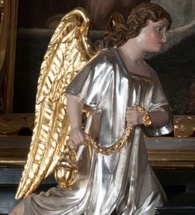 Zdjęcie nr 8: Tabernakulum na rzucie połowy ośmioboku, architektoniczne, na niskim postumencie, trójosiowe, dwudzielne (z wydzieloną gzymsem częścią cokołową), artykułowane kolumienkami o kapitelach kompozytowych oraz wolutami podtrzymującymi kompozytowe kapitele, na wybrzuszonych, zdwojonych cokołach. Belkowanie występujące nad podporami. Ścianka z drzwiczkami zamknięta łukiem półkolistym. Cokoliki, fryz i boczne ścianki tabernakulum zdobione suchym akantem. Drzwiczki jednoskrzydłowe (nowsze, pierwotne dwuskrzydłowe), srebrne, zdobione prostokątną płyciną, z romboidalnymi polami i spłaszczonymi kulami. W narożach stylizowany ornament roślinny. W centrum przedstawienie Chrystusa na krzyżu. Pola bocznych ścianek zdobione imitującymi szufladki mozaikowymi płycinami z różnobarwnych marmurów przedstawiającymi pejzaż z elementami architektury oraz płycinami wykładanymi jasnym drewnem. Pejzażowe płyciny w górnej części tabernakulum ujęte srebrnymi, odlewanymi i cyzelowanym ramkami. 
Na tabernakulum umieszczone antytetycznie rzeźby dwóch aniołów: pełnoplastyczne, w ujęciu całopostaciowym, wolnostojące. Anioł po lewej stronie ukazany jest w pozycji klęczącej, z profilu, pochylony do przodu. W rękach trzyma łódkę na kadzidło. Włosy brązowe, falowane, sięgające do ramion. Twarz pociągła, łukowato wygięte brwi, szeroko otwarte oczy, prosty nos, róż na policzkach. Skrzydła złote. Anioł odziany jest białą tunikę, z krótkimi rękawami i z cienkimi, pionowymi fałdami, załamującymi się na wysokości kolan. Stopy bose. Anioł po prawej ukazany jest w pozycji klęczącej, z profilu, pochylony do przodu. W rękach trzyma trybularz. Włosy brązowe, falowane, sięgające do ramion. Twarz pociągła, łukowato wygięte brwi, szeroko otwarte oczy, prosty nos, róż na policzkach. Skrzydła złote. Anioł odziany jest białą tunikę, z krótkimi rękawami i z cienkimi, pionowymi fałdami, załamującymi się na wysokości kolan. Stopy bose.