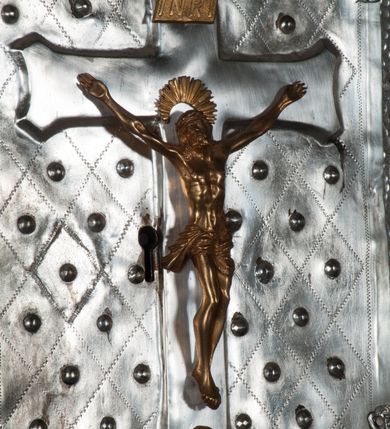 Zdjęcie nr 13: Tabernakulum na rzucie połowy ośmioboku, architektoniczne, na niskim postumencie, trójosiowe, dwudzielne (z wydzieloną gzymsem częścią cokołową), artykułowane kolumienkami o kapitelach kompozytowych oraz wolutami podtrzymującymi kompozytowe kapitele, na wybrzuszonych, zdwojonych cokołach. Belkowanie występujące nad podporami. Ścianka z drzwiczkami zamknięta łukiem półkolistym. Cokoliki, fryz i boczne ścianki tabernakulum zdobione suchym akantem. Drzwiczki jednoskrzydłowe (nowsze, pierwotne dwuskrzydłowe), srebrne, zdobione prostokątną płyciną, z romboidalnymi polami i spłaszczonymi kulami. W narożach stylizowany ornament roślinny. W centrum przedstawienie Chrystusa na krzyżu. Pola bocznych ścianek zdobione imitującymi szufladki mozaikowymi płycinami z różnobarwnych marmurów przedstawiającymi pejzaż z elementami architektury oraz płycinami wykładanymi jasnym drewnem. Pejzażowe płyciny w górnej części tabernakulum ujęte srebrnymi, odlewanymi i cyzelowanym ramkami. 
Na tabernakulum umieszczone antytetycznie rzeźby dwóch aniołów: pełnoplastyczne, w ujęciu całopostaciowym, wolnostojące. Anioł po lewej stronie ukazany jest w pozycji klęczącej, z profilu, pochylony do przodu. W rękach trzyma łódkę na kadzidło. Włosy brązowe, falowane, sięgające do ramion. Twarz pociągła, łukowato wygięte brwi, szeroko otwarte oczy, prosty nos, róż na policzkach. Skrzydła złote. Anioł odziany jest białą tunikę, z krótkimi rękawami i z cienkimi, pionowymi fałdami, załamującymi się na wysokości kolan. Stopy bose. Anioł po prawej ukazany jest w pozycji klęczącej, z profilu, pochylony do przodu. W rękach trzyma trybularz. Włosy brązowe, falowane, sięgające do ramion. Twarz pociągła, łukowato wygięte brwi, szeroko otwarte oczy, prosty nos, róż na policzkach. Skrzydła złote. Anioł odziany jest białą tunikę, z krótkimi rękawami i z cienkimi, pionowymi fałdami, załamującymi się na wysokości kolan. Stopy bose.