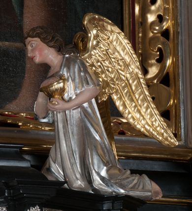 Zdjęcie nr 11: Tabernakulum na rzucie połowy ośmioboku, architektoniczne, na niskim postumencie, trójosiowe, dwudzielne (z wydzieloną gzymsem częścią cokołową), artykułowane kolumienkami o kapitelach kompozytowych oraz wolutami podtrzymującymi kompozytowe kapitele, na wybrzuszonych, zdwojonych cokołach. Belkowanie występujące nad podporami. Ścianka z drzwiczkami zamknięta łukiem półkolistym. Cokoliki, fryz i boczne ścianki tabernakulum zdobione suchym akantem. Drzwiczki jednoskrzydłowe (nowsze, pierwotne dwuskrzydłowe), srebrne, zdobione prostokątną płyciną, z romboidalnymi polami i spłaszczonymi kulami. W narożach stylizowany ornament roślinny. W centrum przedstawienie Chrystusa na krzyżu. Pola bocznych ścianek zdobione imitującymi szufladki mozaikowymi płycinami z różnobarwnych marmurów przedstawiającymi pejzaż z elementami architektury oraz płycinami wykładanymi jasnym drewnem. Pejzażowe płyciny w górnej części tabernakulum ujęte srebrnymi, odlewanymi i cyzelowanym ramkami. 
Na tabernakulum umieszczone antytetycznie rzeźby dwóch aniołów: pełnoplastyczne, w ujęciu całopostaciowym, wolnostojące. Anioł po lewej stronie ukazany jest w pozycji klęczącej, z profilu, pochylony do przodu. W rękach trzyma łódkę na kadzidło. Włosy brązowe, falowane, sięgające do ramion. Twarz pociągła, łukowato wygięte brwi, szeroko otwarte oczy, prosty nos, róż na policzkach. Skrzydła złote. Anioł odziany jest białą tunikę, z krótkimi rękawami i z cienkimi, pionowymi fałdami, załamującymi się na wysokości kolan. Stopy bose. Anioł po prawej ukazany jest w pozycji klęczącej, z profilu, pochylony do przodu. W rękach trzyma trybularz. Włosy brązowe, falowane, sięgające do ramion. Twarz pociągła, łukowato wygięte brwi, szeroko otwarte oczy, prosty nos, róż na policzkach. Skrzydła złote. Anioł odziany jest białą tunikę, z krótkimi rękawami i z cienkimi, pionowymi fałdami, załamującymi się na wysokości kolan. Stopy bose.