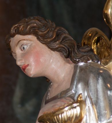 Zdjęcie nr 9: Tabernakulum na rzucie połowy ośmioboku, architektoniczne, na niskim postumencie, trójosiowe, dwudzielne (z wydzieloną gzymsem częścią cokołową), artykułowane kolumienkami o kapitelach kompozytowych oraz wolutami podtrzymującymi kompozytowe kapitele, na wybrzuszonych, zdwojonych cokołach. Belkowanie występujące nad podporami. Ścianka z drzwiczkami zamknięta łukiem półkolistym. Cokoliki, fryz i boczne ścianki tabernakulum zdobione suchym akantem. Drzwiczki jednoskrzydłowe (nowsze, pierwotne dwuskrzydłowe), srebrne, zdobione prostokątną płyciną, z romboidalnymi polami i spłaszczonymi kulami. W narożach stylizowany ornament roślinny. W centrum przedstawienie Chrystusa na krzyżu. Pola bocznych ścianek zdobione imitującymi szufladki mozaikowymi płycinami z różnobarwnych marmurów przedstawiającymi pejzaż z elementami architektury oraz płycinami wykładanymi jasnym drewnem. Pejzażowe płyciny w górnej części tabernakulum ujęte srebrnymi, odlewanymi i cyzelowanym ramkami. 
Na tabernakulum umieszczone antytetycznie rzeźby dwóch aniołów: pełnoplastyczne, w ujęciu całopostaciowym, wolnostojące. Anioł po lewej stronie ukazany jest w pozycji klęczącej, z profilu, pochylony do przodu. W rękach trzyma łódkę na kadzidło. Włosy brązowe, falowane, sięgające do ramion. Twarz pociągła, łukowato wygięte brwi, szeroko otwarte oczy, prosty nos, róż na policzkach. Skrzydła złote. Anioł odziany jest białą tunikę, z krótkimi rękawami i z cienkimi, pionowymi fałdami, załamującymi się na wysokości kolan. Stopy bose. Anioł po prawej ukazany jest w pozycji klęczącej, z profilu, pochylony do przodu. W rękach trzyma trybularz. Włosy brązowe, falowane, sięgające do ramion. Twarz pociągła, łukowato wygięte brwi, szeroko otwarte oczy, prosty nos, róż na policzkach. Skrzydła złote. Anioł odziany jest białą tunikę, z krótkimi rękawami i z cienkimi, pionowymi fałdami, załamującymi się na wysokości kolan. Stopy bose.