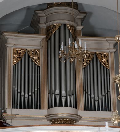 Zdjęcie nr 2: Prospekt architektoniczny, na prostopadłościennym cokole, jednokondygnacyjny, trójosiowy, ze zwieńczeniem. Podziały wewnętrzne wyznaczają kanelowane pilastry wspierające uproszczone belkowanie i gzyms. Część środkowa prospektu występująca półkoliście przed lico, wypiętrzona w stosunku do części skrajnych, zwieńczona rzeźbionym złoconym ornamentem o motywach roślinnych. Pola skrajne prostokątne. Górne naroża otworów na piszczałki wypełnione ażurowymi, złoconymi motywami liści akantu. Struktura malowana na biało, detale architektoniczne i ornamenty złocone. Pierwotnie na narożach złocone wazony. 