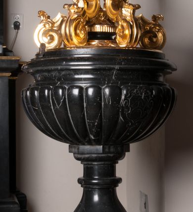 Zdjęcie nr 3: Chrzcielnica stoi na okrągłym postumencie i wyżej ośmiobocznej podstawie. Składa się z trzonu w typie gruszkowym i czary półkulistej, puklowanej, z profilowanym brzegiem. Na czarze wypukłorzeźbiony kartusz z tarczą z herbem Ogończyk i syglami Z[YGMUNT] O[GOŃCZYK] P[ROBOSZCZ] R[USIECKI]. Pokrywa drewniana, utworzona z sześciu faliście kształtowanych spływów wolutowych ozdobionych liśćmi, podtrzymujących koronę zamkniętą z sześcioma kabłąkami zwieńczonymi kulą z krzyżem. Obręcz korony z imitacją kamieni szlachetnych, zdobiona w górnej części perełkowaniem. U nasady kabłąków znajdują się rozłożyste kwiaty, od wewnątrz kabłąki pomalowane czerwoną farbą imitującą tkaninę. 