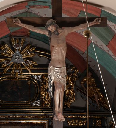 Zdjęcie nr 3: Chrystus wiszący na ramionach łagodnym łukiem rozpostartych na krzyżu, o smukłej sylwecie, z nogami skrzyżowanymi, lekko ugiętymi w kolanach. Ciało zmarłego Chrystusa ukazane jest realistycznie, z głową silnie przechyloną na prawe ramie, zamkniętymi oczami, długim nosem i otwartymi ustami. Twarz okala krótka, spiczasta broda i wąsy, włosy opadają na kark i klatkę piersiową, na głowie korona cierniowa w kształcie skręconego sznura z kolcami. Klatka piersiowa o owalnym obrysie, z zaznaczonymi żebrami. Stosunkowo długie perizonium, zdobione srebrzeniem na pulmencie, układa się z przodu łukowatymi fałdami i spływa z bioder dekoracyjnie traktowanymi zwisami. Na ciele widoczna rana od włóczni, z niej i z ran na rękach i nogach widoczne spływające strużki krwi. 
