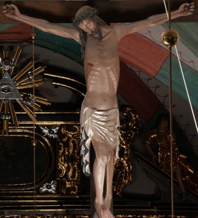 Zdjęcie nr 1: Chrystus wiszący na ramionach łagodnym łukiem rozpostartych na krzyżu, o smukłej sylwecie, z nogami skrzyżowanymi, lekko ugiętymi w kolanach. Ciało zmarłego Chrystusa ukazane jest realistycznie, z głową silnie przechyloną na prawe ramie, zamkniętymi oczami, długim nosem i otwartymi ustami. Twarz okala krótka, spiczasta broda i wąsy, włosy opadają na kark i klatkę piersiową, na głowie korona cierniowa w kształcie skręconego sznura z kolcami. Klatka piersiowa o owalnym obrysie, z zaznaczonymi żebrami. Stosunkowo długie perizonium, zdobione srebrzeniem na pulmencie, układa się z przodu łukowatymi fałdami i spływa z bioder dekoracyjnie traktowanymi zwisami. Na ciele widoczna rana od włóczni, z niej i z ran na rękach i nogach widoczne spływające strużki krwi. 
