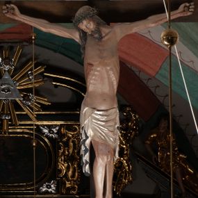 Zdjęcie nr 1: Chrystus wiszący na ramionach łagodnym łukiem rozpostartych na krzyżu, o smukłej sylwecie, z nogami skrzyżowanymi, lekko ugiętymi w kolanach. Ciało zmarłego Chrystusa ukazane jest realistycznie, z głową silnie przechyloną na prawe ramie, zamkniętymi oczami, długim nosem i otwartymi ustami. Twarz okala krótka, spiczasta broda i wąsy, włosy opadają na kark i klatkę piersiową, na głowie korona cierniowa w kształcie skręconego sznura z kolcami. Klatka piersiowa o owalnym obrysie, z zaznaczonymi żebrami. Stosunkowo długie perizonium, zdobione srebrzeniem na pulmencie, układa się z przodu łukowatymi fałdami i spływa z bioder dekoracyjnie traktowanymi zwisami. Na ciele widoczna rana od włóczni, z niej i z ran na rękach i nogach widoczne spływające strużki krwi. 

