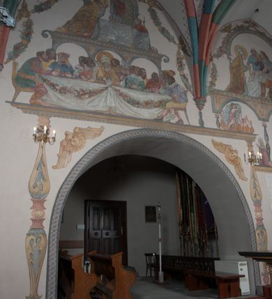 Zdjęcie nr 43: Sklepienie: żebra ozdobione na przemian pasami w kolorach czerwonym i niebieskim. Na gładkich zwornikach malowane tarcze herbowe od wschodu: Gryf i Łabędź. Wysklepki malowane wzdłuż żeber ornamentem geometrycznym złożonym z półkoli, zakończonych liliami heraldycznymi. Ze zworników rozchodzi się wić roślinna.
Ściana północna: przęsło wschodnie - trzy sceny podzielone na dwie strefy, zamknięte arkadami wspartymi na tralkach. W dolnej: klęczący św. Grzegorz, pod arkadą, na tle tkaniny; w kolejnej postać klęczącej kobiety przed sceną zstąpienia Chrystusa do piekieł (?). W górnej strefie św. Grzegorz klęczący przed trzema mężczyznami zgrupowanymi wokół stołu, którzy pokazują świętemu tkaninę. Przęsło zachodnie: scena podzielone na dwie strefy. W dolnej scena wielofiguralna, przedstawiająca ucztę ze św. Grzegorzem z gołębicą na ramieniu, siedzącym po środku stołu, oraz z pochylającym się ku niemu aniołem. Zamykają ją trzy arkady. W górnej scena eucharystyczna ze św. Grzegorzem i diakonem, klęczącymi przed ołtarzem, na którym stoi Chrystus na tle niszy. Całość zamknięta arkadą. Łuk arkady prowadzącej do kruchty podkreślony bordiurą z ornamentem plecionkowym, ujęty kandelabrami dźwigającymi gzyms. W przyłuczach dwie uskrzydlone główki anielskie. Ściana południowa: W obu przęsłach analogicznie do okien malowane iluzjonistyczne nisze konchowe z postaciami świętych na postumentach w górnej strefie ściany. W podłuczach arkad girlandy, podtrzymywane przez uskrzydlone główki anielskie. Nisze i okna obwiedzione bordiurą z ornamentem geometrycznym, podtrzymane wspólnym parapetem z podwieszoną girlandą kwiatową. Pod wspornikiem malowana kolumna utworzona z dwóch tralek. W prześle wschodnim: postać św. Wojciecha, z malowaną na postumencie inskrypcją: ŚW. WOJCIECH / PIERWSZY MĘCZNNIK POLSKI. W przęśle zachodnim: postać św. Stanisława biskupa z półpostacią Piotrowina z prawej strony. Na postumencie malowana inskrypcja: W 700-LECIE KANONIZACJI / ŚW. STANISŁAWA BP-A KRAKOWSKIEGO / 1253 – 1953.W dolnej strefie ściany epitafia ujmuje dekoracja. Epitafium Jacka Konstantyna Chościaka Popiela: stylizowane dekoracja roślinna z falującymi wstęgami; tablica pamiątkowa podtrzymywana przez putta. Łuk tęczowy od strony prezbiterium obwiedziony analogicznym do sklepienia geometrycznym ornamentem. Kolorystyka pastelowa, z silnymi akcentami błękitu, czerwieni i żółcieni.