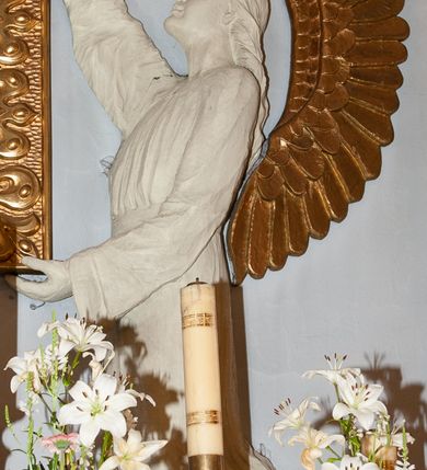 Zdjęcie nr 8: Nastawa niearchitektoniczna. Ołtarz prostopadłościenny, kamienny, z drewnianą mensą. Antepedium dekorowane trzema kwadratowymi polami wypełnionymi geometryczną mozaiką w formie krzyży o rozszerzających się ramionach. Na ołtarzu tabernakulum w formie prostopadłościennej skrzynki, obitej blachą, o zaokrąglonych narożach. Drzwiczki w kształcie stojącego prostokąta zamkniętego łukiem półkolistym nadwieszonym, z przedstawieniem kielicha z hostią w glorii. Na ściance frontowej aplikowana dekoracja w postaci kłosów zbóż i winnego grona. Tron wystawienia w formie baldachimu podtrzymywanego na czterech tralkach. Obraz Matki Boskiej Częstochowskiej w kształcie stojącego prostokąta, ujęty grubą, złoconą ramą dekorowaną ornamentem z lilii heraldycznych. Dzieło flankowane jest dwiema postaciami klęczących aniołów, podtrzymujących je obiema rękami. Anioły ukazane z profilu, lewy z głową skierowaną frontalnie. Ubrane są w luźne tuniki przepasane w talii. Skrzydła mają duże, złożone, wygięte na kształt litery „C”. Nad obrazem monogram Marii, flankowany przez dwa putta podtrzymujące nad nim koronę otwartą. Postacie polichromowane są na biało, o złoconych skrzydłach. 

