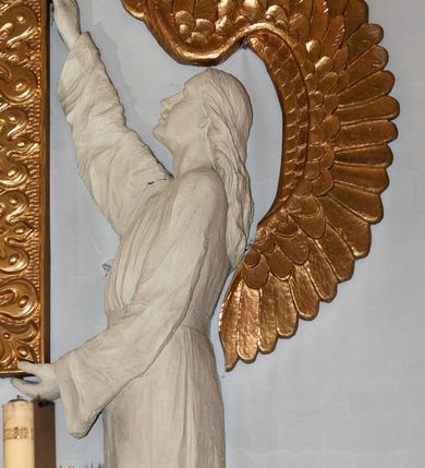 Zdjęcie nr 6: Nastawa niearchitektoniczna. Ołtarz prostopadłościenny, kamienny, z drewnianą mensą. Antepedium dekorowane trzema kwadratowymi polami wypełnionymi geometryczną mozaiką w formie krzyży o rozszerzających się ramionach. Na ołtarzu tabernakulum w formie prostopadłościennej skrzynki, obitej blachą, o zaokrąglonych narożach. Drzwiczki w kształcie stojącego prostokąta zamkniętego łukiem półkolistym nadwieszonym, z przedstawieniem kielicha z hostią w glorii. Na ściance frontowej aplikowana dekoracja w postaci kłosów zbóż i winnego grona. Tron wystawienia w formie baldachimu podtrzymywanego na czterech tralkach. Obraz Matki Boskiej Częstochowskiej w kształcie stojącego prostokąta, ujęty grubą, złoconą ramą dekorowaną ornamentem z lilii heraldycznych. Dzieło flankowane jest dwiema postaciami klęczących aniołów, podtrzymujących je obiema rękami. Anioły ukazane z profilu, lewy z głową skierowaną frontalnie. Ubrane są w luźne tuniki przepasane w talii. Skrzydła mają duże, złożone, wygięte na kształt litery „C”. Nad obrazem monogram Marii, flankowany przez dwa putta podtrzymujące nad nim koronę otwartą. Postacie polichromowane są na biało, o złoconych skrzydłach. 

