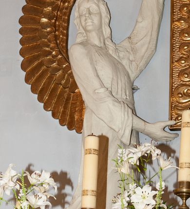 Zdjęcie nr 7: Nastawa niearchitektoniczna. Ołtarz prostopadłościenny, kamienny, z drewnianą mensą. Antepedium dekorowane trzema kwadratowymi polami wypełnionymi geometryczną mozaiką w formie krzyży o rozszerzających się ramionach. Na ołtarzu tabernakulum w formie prostopadłościennej skrzynki, obitej blachą, o zaokrąglonych narożach. Drzwiczki w kształcie stojącego prostokąta zamkniętego łukiem półkolistym nadwieszonym, z przedstawieniem kielicha z hostią w glorii. Na ściance frontowej aplikowana dekoracja w postaci kłosów zbóż i winnego grona. Tron wystawienia w formie baldachimu podtrzymywanego na czterech tralkach. Obraz Matki Boskiej Częstochowskiej w kształcie stojącego prostokąta, ujęty grubą, złoconą ramą dekorowaną ornamentem z lilii heraldycznych. Dzieło flankowane jest dwiema postaciami klęczących aniołów, podtrzymujących je obiema rękami. Anioły ukazane z profilu, lewy z głową skierowaną frontalnie. Ubrane są w luźne tuniki przepasane w talii. Skrzydła mają duże, złożone, wygięte na kształt litery „C”. Nad obrazem monogram Marii, flankowany przez dwa putta podtrzymujące nad nim koronę otwartą. Postacie polichromowane są na biało, o złoconych skrzydłach. 

