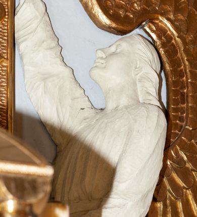 Zdjęcie nr 9: Nastawa niearchitektoniczna. Ołtarz prostopadłościenny, kamienny, z drewnianą mensą. Antepedium dekorowane trzema kwadratowymi polami wypełnionymi geometryczną mozaiką w formie krzyży o rozszerzających się ramionach. Na ołtarzu tabernakulum w formie prostopadłościennej skrzynki, obitej blachą, o zaokrąglonych narożach. Drzwiczki w kształcie stojącego prostokąta zamkniętego łukiem półkolistym nadwieszonym, z przedstawieniem kielicha z hostią w glorii. Na ściance frontowej aplikowana dekoracja w postaci kłosów zbóż i winnego grona. Tron wystawienia w formie baldachimu podtrzymywanego na czterech tralkach. Obraz Matki Boskiej Częstochowskiej w kształcie stojącego prostokąta, ujęty grubą, złoconą ramą dekorowaną ornamentem z lilii heraldycznych. Dzieło flankowane jest dwiema postaciami klęczących aniołów, podtrzymujących je obiema rękami. Anioły ukazane z profilu, lewy z głową skierowaną frontalnie. Ubrane są w luźne tuniki przepasane w talii. Skrzydła mają duże, złożone, wygięte na kształt litery „C”. Nad obrazem monogram Marii, flankowany przez dwa putta podtrzymujące nad nim koronę otwartą. Postacie polichromowane są na biało, o złoconych skrzydłach. 

