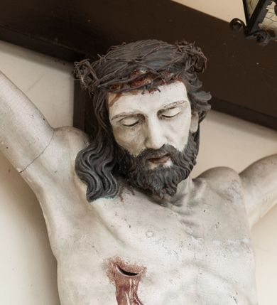 Zdjęcie nr 3: Na skrzyżowaniu ramion postać zmarłego Chrystusa, przybitego trzema gwoździami do krzyża. Ciało w delikatnym zwisie, o szeroko rozłożonych ramionach i rozciągniętej, prostej sylwetce. Głowa w koronie cierniowej opada na prawe ramię. Twarz o precyzyjnie oddanych rysach, okolona zarostem; włosy w postaci pukli opadają na plecy i prawe ramię. Ciało oddane z dbałością o detale anatomiczne, z zaznaczonymi śladami męki – krwią wypływającą z miejsc przebić i z rany na prawym boku. Białe perizonium w formie tkaniny opasującej biodra, drapowanej w spływające ku ziemi fałdy, z węzłem i zwisem na prawym boku. Titulus w kształcie banderoli z napisem „INRI”. Polichromia w partiach ciała naturalistyczna.