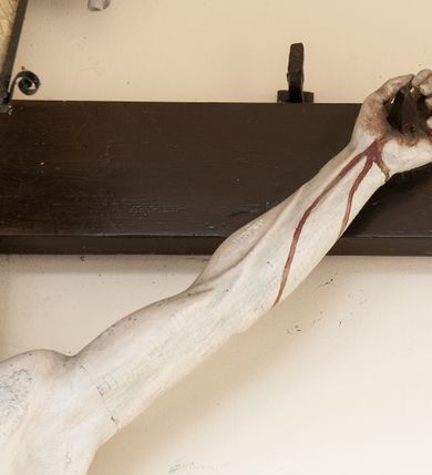 Zdjęcie nr 5: Na skrzyżowaniu ramion postać zmarłego Chrystusa, przybitego trzema gwoździami do krzyża. Ciało w delikatnym zwisie, o szeroko rozłożonych ramionach i rozciągniętej, prostej sylwetce. Głowa w koronie cierniowej opada na prawe ramię. Twarz o precyzyjnie oddanych rysach, okolona zarostem; włosy w postaci pukli opadają na plecy i prawe ramię. Ciało oddane z dbałością o detale anatomiczne, z zaznaczonymi śladami męki – krwią wypływającą z miejsc przebić i z rany na prawym boku. Białe perizonium w formie tkaniny opasującej biodra, drapowanej w spływające ku ziemi fałdy, z węzłem i zwisem na prawym boku. Titulus w kształcie banderoli z napisem „INRI”. Polichromia w partiach ciała naturalistyczna.