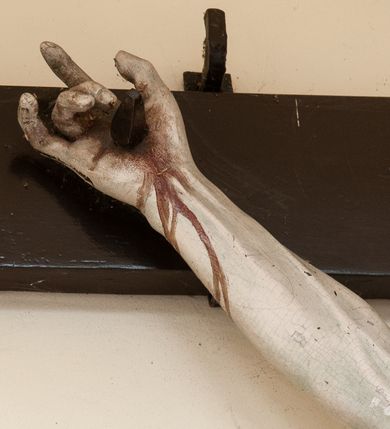 Zdjęcie nr 6: Na skrzyżowaniu ramion postać zmarłego Chrystusa, przybitego trzema gwoździami do krzyża. Ciało w delikatnym zwisie, o szeroko rozłożonych ramionach i rozciągniętej, prostej sylwetce. Głowa w koronie cierniowej opada na prawe ramię. Twarz o precyzyjnie oddanych rysach, okolona zarostem; włosy w postaci pukli opadają na plecy i prawe ramię. Ciało oddane z dbałością o detale anatomiczne, z zaznaczonymi śladami męki – krwią wypływającą z miejsc przebić i z rany na prawym boku. Białe perizonium w formie tkaniny opasującej biodra, drapowanej w spływające ku ziemi fałdy, z węzłem i zwisem na prawym boku. Titulus w kształcie banderoli z napisem „INRI”. Polichromia w partiach ciała naturalistyczna.