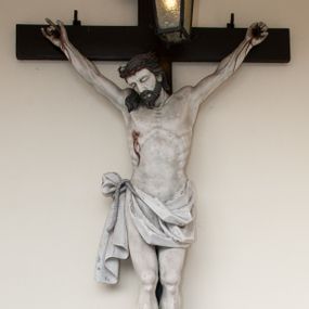 Zdjęcie nr 1: Na skrzyżowaniu ramion postać zmarłego Chrystusa, przybitego trzema gwoździami do krzyża. Ciało w delikatnym zwisie, o szeroko rozłożonych ramionach i rozciągniętej, prostej sylwetce. Głowa w koronie cierniowej opada na prawe ramię. Twarz o precyzyjnie oddanych rysach, okolona zarostem; włosy w postaci pukli opadają na plecy i prawe ramię. Ciało oddane z dbałością o detale anatomiczne, z zaznaczonymi śladami męki – krwią wypływającą z miejsc przebić i z rany na prawym boku. Białe perizonium w formie tkaniny opasującej biodra, drapowanej w spływające ku ziemi fałdy, z węzłem i zwisem na prawym boku. Titulus w kształcie banderoli z napisem „INRI”. Polichromia w partiach ciała naturalistyczna.
