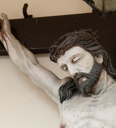 Zdjęcie nr 4: Na skrzyżowaniu ramion postać zmarłego Chrystusa, przybitego trzema gwoździami do krzyża. Ciało w delikatnym zwisie, o szeroko rozłożonych ramionach i rozciągniętej, prostej sylwetce. Głowa w koronie cierniowej opada na prawe ramię. Twarz o precyzyjnie oddanych rysach, okolona zarostem; włosy w postaci pukli opadają na plecy i prawe ramię. Ciało oddane z dbałością o detale anatomiczne, z zaznaczonymi śladami męki – krwią wypływającą z miejsc przebić i z rany na prawym boku. Białe perizonium w formie tkaniny opasującej biodra, drapowanej w spływające ku ziemi fałdy, z węzłem i zwisem na prawym boku. Titulus w kształcie banderoli z napisem „INRI”. Polichromia w partiach ciała naturalistyczna.