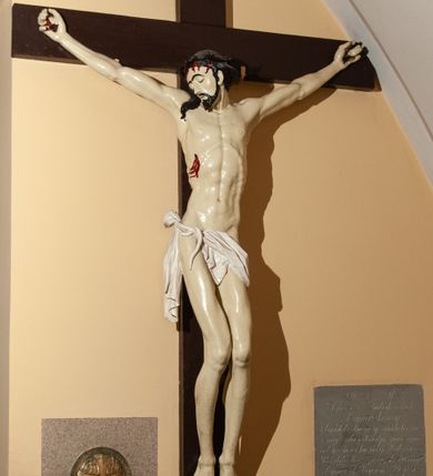 Zdjęcie nr 1: Wizerunek Chrystusa przybitego czterema gwoździami do krzyża. Ciało  szczupłe, wydłużone, wyprostowane, o wyraźnie zaznaczonej linii żeber, długie ręce rozciągnięte powyżej głowy, nogi delikatnie ugięte w kolanach, stopy przybite obok siebie. Głowa opada na prawy bark. Jezus ma podłużną, szczupłą twarz, oczy zamknięte, usta rozchylone, nos prosty. Na jasnej karnacji silnie odznaczają się ciemne brwi, krótkie wąsy oraz broda. Układające się w fale włosy opadają na plecy i prawy bark. Na głowie cienka, czarna korona cierniowa. Biodra otacza białe perizonium ułożone w sztywne fałdy, przewinięte z przodu i zwisające przy prawym udzie, przytrzymane sznurem przewiniętym na prawym boku. W miejscach przebić gwoździami, przy koronie cierniowej oraz w ranie w boku ślady krwi. Krzyż gładki, ciemnobrązowy, na górnej belce titulus w formie rozwiniętego zwoju z literami „IN/RI” (łac. Iesus Nazarenus Rex Iudaeorum). Polichromia w partiach ciała naturalistyczna.