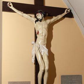 Zdjęcie nr 1: Wizerunek Chrystusa przybitego czterema gwoździami do krzyża. Ciało  szczupłe, wydłużone, wyprostowane, o wyraźnie zaznaczonej linii żeber, długie ręce rozciągnięte powyżej głowy, nogi delikatnie ugięte w kolanach, stopy przybite obok siebie. Głowa opada na prawy bark. Jezus ma podłużną, szczupłą twarz, oczy zamknięte, usta rozchylone, nos prosty. Na jasnej karnacji silnie odznaczają się ciemne brwi, krótkie wąsy oraz broda. Układające się w fale włosy opadają na plecy i prawy bark. Na głowie cienka, czarna korona cierniowa. Biodra otacza białe perizonium ułożone w sztywne fałdy, przewinięte z przodu i zwisające przy prawym udzie, przytrzymane sznurem przewiniętym na prawym boku. W miejscach przebić gwoździami, przy koronie cierniowej oraz w ranie w boku ślady krwi. Krzyż gładki, ciemnobrązowy, na górnej belce titulus w formie rozwiniętego zwoju z literami „IN/RI” (łac. Iesus Nazarenus Rex Iudaeorum). Polichromia w partiach ciała naturalistyczna.