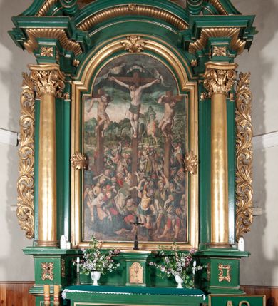 Zdjęcie nr 1: Ołtarz przyścienny, architektoniczny, jednoosiowy, jednokondygnacyjny, z uszakami. Mensa prostopadłościenna. Na niej prostopadłościenne tabernakulum zwieńczone wydatnym gzymsem, z drzwiczkami zamkniętymi łukiem nadwieszonym z motywem kielicha z hostią. Nastawa ołtarzowa ujęta korynckimi kolumnami ustawionymi na podwójnym cokole zdobionym prostokątnymi płycinami w dolnej partii i plakietami utworzonymi z ornamentu małżowinowo-chrząstkowego w górnej. Podpory dźwigają pełne, wyłamane na ich osiach belkowanie, którego gzyms jest wyniesiony nad polem centralnym. Fryz wysuniętych części dekorowany rozetami, silnie wystający gzyms zdobiony wałeczkami. Na wyłamanych częściach belkowania ustawiono symetrycznie woluty. W polu nisza zamknięta łukiem półkolistym nadwieszonym mieszcząca obraz z wielopostaciową sceną Ukrzyżowania w profilowanej ramie dekorowanej w trzech miejscach ornamentem roślinnym. Kondygnacja ujęta ażurowymi uszakami utworzonymi z suchej wici akantu. Struktura ołtarza w kolorze zielonym, trzony kolumn, detale i ornamenty złocone.