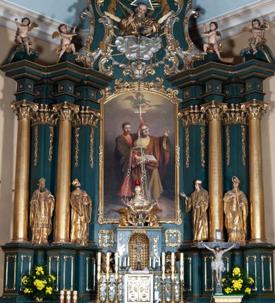 Zdjęcie nr 1: Ołtarz architektoniczny, jednoosiowy, jednokondygnacyjny ze zwieńczeniem, na podwójnym cokole. Mensa prostopadłościenna z antepedium dekorowanym płaskorzeźbionym przedstawieniem Jezusa rozdającego Komunię Świętą. Tabernakulum złożone z prostopadłościennej, obitej blachą skrzynki z drzwiczkami dekorowanymi literami „A” i „Ω” w górnej części i tablicami Dekalogu i otwartą księgą w dolnej, ujętymi winną latoroślą. Skrzynkę flankują prostopadłościany dekorowane na frontowych ściankach symbolami wiary i narzędziami męki, na których umieszczono klęczące, modlące się anioły. Między nimi ustawiono tron wystawienia w formie kolejnego prostopadłościanu, w którego frontowej ścianie znajduje się nisza wyłożona kratką z rozetami i ujęta dekoracją złożoną z księgi, tablic 10 przykazań i winnej latorośli.  Tron wystawienia zwieńczony gzymsem i postaciami dwóch aniołów, które klęczą i pochylają się w modlitewnych gestach. Oś nastawy flankują na przemian dwie pary pilastrów i dwie pary kolumn o kapitelach kompozytowych, ustawionych ukośnie względem lica ołtarza. Pomiędzy nimi znajdują się cztery figury (od lewej): św. Wojciecha, św. Jana Kantego, św. Kazimierza Jagiellończyka i św. Stanisława. W polu środkowym obraz z przedstawieniem świętych patronów Szymona i Judy Tadeusza w formie stojącego prostokąta zamkniętego łukiem odcinkowym w profilowanej, złoconej ramie ozdobionej rocaille’em. U spodu dwie ornamentalne ramki z motywem winnego grona z kluczami Piotrowymi po prawej i krzyżem ze stułą i lilią, po lewej. Kolumny dźwigają wyłamane belkowanie, przerwane w partii środkowej. Górną partię belkowania na osiach kolumn wieńczą putta posadowione na wolutach. Cokół dekorowany płycinami z rocaille’em, trzony pilastrów festonami utworzonymi z wstęgi i kiści winnego grona. W partii fryzu płyciny z rozetami. Fantazyjne zwieńczenie w formie zbliżonej do stojącego prostokąta. W nim, na obłoku półpostać błogosławiącego Boga Ojca w trójkątnym nimbie, z jabłkiem królewskim w formie globu zwieńczonego krzyżem w lewej dłoni. Poniżej gołębica Ducha Świętego w glorii promienistej. Kondygnacje od zwieńczenia oddziela kartusz utworzony z ornamentu rocaille’owego i wstęgi. Struktura polichromowana na kolor ciemnoniebieski, ze złoconą ornamentyką i złoconymi i srebrzonymi detalami.