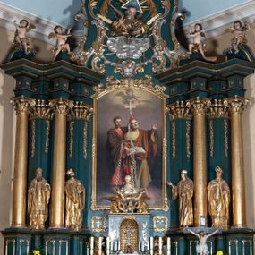 Zdjęcie nr 1: Ołtarz architektoniczny, jednoosiowy, jednokondygnacyjny ze zwieńczeniem, na podwójnym cokole. Mensa prostopadłościenna z antepedium dekorowanym płaskorzeźbionym przedstawieniem Jezusa rozdającego Komunię Świętą. Tabernakulum złożone z prostopadłościennej, obitej blachą skrzynki z drzwiczkami dekorowanymi literami „A” i „Ω” w górnej części i tablicami Dekalogu i otwartą księgą w dolnej, ujętymi winną latoroślą. Skrzynkę flankują prostopadłościany dekorowane na frontowych ściankach symbolami wiary i narzędziami męki, na których umieszczono klęczące, modlące się anioły. Między nimi ustawiono tron wystawienia w formie kolejnego prostopadłościanu, w którego frontowej ścianie znajduje się nisza wyłożona kratką z rozetami i ujęta dekoracją złożoną z księgi, tablic 10 przykazań i winnej latorośli.  Tron wystawienia zwieńczony gzymsem i postaciami dwóch aniołów, które klęczą i pochylają się w modlitewnych gestach. Oś nastawy flankują na przemian dwie pary pilastrów i dwie pary kolumn o kapitelach kompozytowych, ustawionych ukośnie względem lica ołtarza. Pomiędzy nimi znajdują się cztery figury (od lewej): św. Wojciecha, św. Jana Kantego, św. Kazimierza Jagiellończyka i św. Stanisława. W polu środkowym obraz z przedstawieniem świętych patronów Szymona i Judy Tadeusza w formie stojącego prostokąta zamkniętego łukiem odcinkowym w profilowanej, złoconej ramie ozdobionej rocaille’em. U spodu dwie ornamentalne ramki z motywem winnego grona z kluczami Piotrowymi po prawej i krzyżem ze stułą i lilią, po lewej. Kolumny dźwigają wyłamane belkowanie, przerwane w partii środkowej. Górną partię belkowania na osiach kolumn wieńczą putta posadowione na wolutach. Cokół dekorowany płycinami z rocaille’em, trzony pilastrów festonami utworzonymi z wstęgi i kiści winnego grona. W partii fryzu płyciny z rozetami. Fantazyjne zwieńczenie w formie zbliżonej do stojącego prostokąta. W nim, na obłoku półpostać błogosławiącego Boga Ojca w trójkątnym nimbie, z jabłkiem królewskim w formie globu zwieńczonego krzyżem w lewej dłoni. Poniżej gołębica Ducha Świętego w glorii promienistej. Kondygnacje od zwieńczenia oddziela kartusz utworzony z ornamentu rocaille’owego i wstęgi. Struktura polichromowana na kolor ciemnoniebieski, ze złoconą ornamentyką i złoconymi i srebrzonymi detalami.