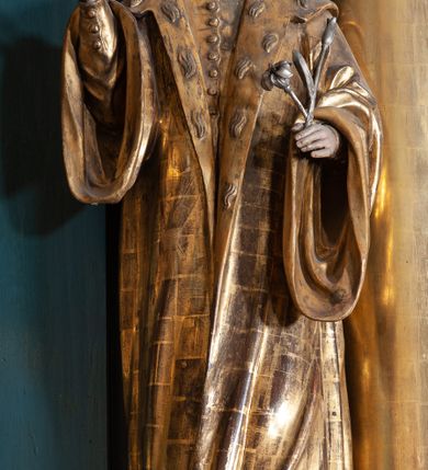 Zdjęcie nr 10: Ołtarz architektoniczny, jednoosiowy, jednokondygnacyjny ze zwieńczeniem, na podwójnym cokole. Mensa prostopadłościenna z antepedium dekorowanym płaskorzeźbionym przedstawieniem Jezusa rozdającego Komunię Świętą. Tabernakulum złożone z prostopadłościennej, obitej blachą skrzynki z drzwiczkami dekorowanymi literami „A” i „Ω” w górnej części i tablicami Dekalogu i otwartą księgą w dolnej, ujętymi winną latoroślą. Skrzynkę flankują prostopadłościany dekorowane na frontowych ściankach symbolami wiary i narzędziami męki, na których umieszczono klęczące, modlące się anioły. Między nimi ustawiono tron wystawienia w formie kolejnego prostopadłościanu, w którego frontowej ścianie znajduje się nisza wyłożona kratką z rozetami i ujęta dekoracją złożoną z księgi, tablic 10 przykazań i winnej latorośli.  Tron wystawienia zwieńczony gzymsem i postaciami dwóch aniołów, które klęczą i pochylają się w modlitewnych gestach. Oś nastawy flankują na przemian dwie pary pilastrów i dwie pary kolumn o kapitelach kompozytowych, ustawionych ukośnie względem lica ołtarza. Pomiędzy nimi znajdują się cztery figury (od lewej): św. Wojciecha, św. Jana Kantego, św. Kazimierza Jagiellończyka i św. Stanisława. W polu środkowym obraz z przedstawieniem świętych patronów Szymona i Judy Tadeusza w formie stojącego prostokąta zamkniętego łukiem odcinkowym w profilowanej, złoconej ramie ozdobionej rocaille’em. U spodu dwie ornamentalne ramki z motywem winnego grona z kluczami Piotrowymi po prawej i krzyżem ze stułą i lilią, po lewej. Kolumny dźwigają wyłamane belkowanie, przerwane w partii środkowej. Górną partię belkowania na osiach kolumn wieńczą putta posadowione na wolutach. Cokół dekorowany płycinami z rocaille’em, trzony pilastrów festonami utworzonymi z wstęgi i kiści winnego grona. W partii fryzu płyciny z rozetami. Fantazyjne zwieńczenie w formie zbliżonej do stojącego prostokąta. W nim, na obłoku półpostać błogosławiącego Boga Ojca w trójkątnym nimbie, z jabłkiem królewskim w formie globu zwieńczonego krzyżem w lewej dłoni. Poniżej gołębica Ducha Świętego w glorii promienistej. Kondygnacje od zwieńczenia oddziela kartusz utworzony z ornamentu rocaille’owego i wstęgi. Struktura polichromowana na kolor ciemnoniebieski, ze złoconą ornamentyką i złoconymi i srebrzonymi detalami.