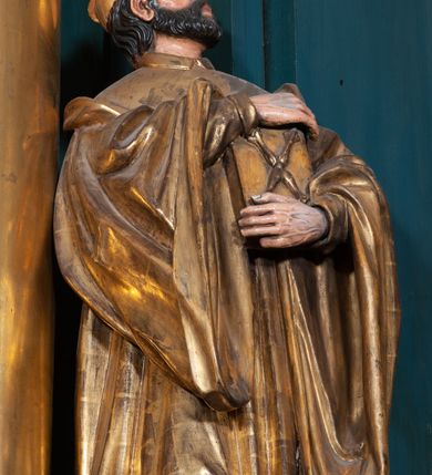 Zdjęcie nr 9: Ołtarz architektoniczny, jednoosiowy, jednokondygnacyjny ze zwieńczeniem, na podwójnym cokole. Mensa prostopadłościenna z antepedium dekorowanym płaskorzeźbionym przedstawieniem Jezusa rozdającego Komunię Świętą. Tabernakulum złożone z prostopadłościennej, obitej blachą skrzynki z drzwiczkami dekorowanymi literami „A” i „Ω” w górnej części i tablicami Dekalogu i otwartą księgą w dolnej, ujętymi winną latoroślą. Skrzynkę flankują prostopadłościany dekorowane na frontowych ściankach symbolami wiary i narzędziami męki, na których umieszczono klęczące, modlące się anioły. Między nimi ustawiono tron wystawienia w formie kolejnego prostopadłościanu, w którego frontowej ścianie znajduje się nisza wyłożona kratką z rozetami i ujęta dekoracją złożoną z księgi, tablic 10 przykazań i winnej latorośli.  Tron wystawienia zwieńczony gzymsem i postaciami dwóch aniołów, które klęczą i pochylają się w modlitewnych gestach. Oś nastawy flankują na przemian dwie pary pilastrów i dwie pary kolumn o kapitelach kompozytowych, ustawionych ukośnie względem lica ołtarza. Pomiędzy nimi znajdują się cztery figury (od lewej): św. Wojciecha, św. Jana Kantego, św. Kazimierza Jagiellończyka i św. Stanisława. W polu środkowym obraz z przedstawieniem świętych patronów Szymona i Judy Tadeusza w formie stojącego prostokąta zamkniętego łukiem odcinkowym w profilowanej, złoconej ramie ozdobionej rocaille’em. U spodu dwie ornamentalne ramki z motywem winnego grona z kluczami Piotrowymi po prawej i krzyżem ze stułą i lilią, po lewej. Kolumny dźwigają wyłamane belkowanie, przerwane w partii środkowej. Górną partię belkowania na osiach kolumn wieńczą putta posadowione na wolutach. Cokół dekorowany płycinami z rocaille’em, trzony pilastrów festonami utworzonymi z wstęgi i kiści winnego grona. W partii fryzu płyciny z rozetami. Fantazyjne zwieńczenie w formie zbliżonej do stojącego prostokąta. W nim, na obłoku półpostać błogosławiącego Boga Ojca w trójkątnym nimbie, z jabłkiem królewskim w formie globu zwieńczonego krzyżem w lewej dłoni. Poniżej gołębica Ducha Świętego w glorii promienistej. Kondygnacje od zwieńczenia oddziela kartusz utworzony z ornamentu rocaille’owego i wstęgi. Struktura polichromowana na kolor ciemnoniebieski, ze złoconą ornamentyką i złoconymi i srebrzonymi detalami.