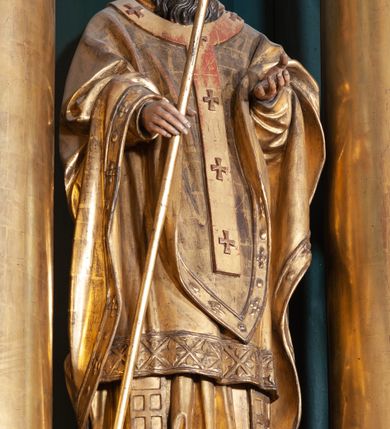 Zdjęcie nr 2: Figura ścięta z tyłu, na cokole. Święty Wojciech został ukazany w pozycji stojącej z uniesionymi rękami, w prawej trzyma krzyż misyjny. Twarz ma pociągłą, brwi wąskie, oczy szeroko otwarte, głęboko osadzone, nos prosty, wąski i długą, sięgającą dekoltu brodę. Jest ubrany w sutannę, komżę, ornat, stułę i paliusz; na głowie ma infułę. Polichromia w partiach ciała naturalistyczna, szaty i atrybuty złocone. 