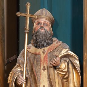 Zdjęcie nr 1: Figura ścięta z tyłu, na cokole. Święty Wojciech został ukazany w pozycji stojącej z uniesionymi rękami, w prawej trzyma krzyż misyjny. Twarz ma pociągłą, brwi wąskie, oczy szeroko otwarte, głęboko osadzone, nos prosty, wąski i długą, sięgającą dekoltu brodę. Jest ubrany w sutannę, komżę, ornat, stułę i paliusz; na głowie ma infułę. Polichromia w partiach ciała naturalistyczna, szaty i atrybuty złocone. 