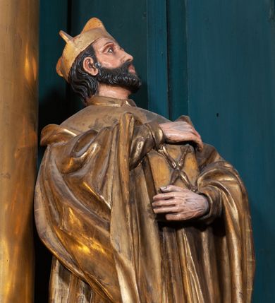 Zdjęcie nr 1: Rzeźba ścięta z tyłu, na cokole, przedstawiająca św. Jana Kantego ukazanego w całej postaci, zwróconego nieznacznie w lewo. Święty obiema rękami przyciska do ciała zamkniętą księgę ze skrzyżowanymi berłami, godłem Uniwersytetu Krakowskiego na okładce. Spogląda w górę, ma owalną, szczupłą twarz z dużymi, szeroko otwartymi oczami i prostym nosem, okalają ją ciemnobrązowe, krótkie, zaczesane do tyłu włosy. Święty ma krótką brodę oraz wąsy. Jest ubrany w obszerną togę uniwersytecką z szerokimi rękawami, które sięgają ud. Na głowie ma biret. Tkanina płaszcza spływa do ziemi podłużnymi, równoległymi fałdami. W partiach ciała polichromia naturalistyczna, płaszcz i atrybuty złocone.