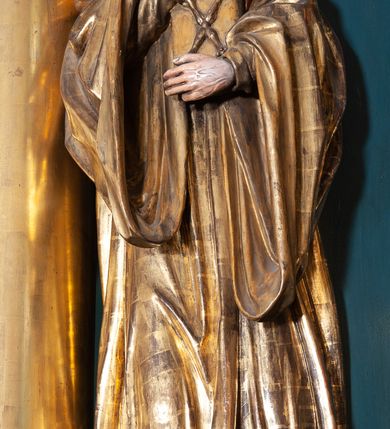 Zdjęcie nr 2: Rzeźba ścięta z tyłu, na cokole, przedstawiająca św. Jana Kantego ukazanego w całej postaci, zwróconego nieznacznie w lewo. Święty obiema rękami przyciska do ciała zamkniętą księgę ze skrzyżowanymi berłami, godłem Uniwersytetu Krakowskiego na okładce. Spogląda w górę, ma owalną, szczupłą twarz z dużymi, szeroko otwartymi oczami i prostym nosem, okalają ją ciemnobrązowe, krótkie, zaczesane do tyłu włosy. Święty ma krótką brodę oraz wąsy. Jest ubrany w obszerną togę uniwersytecką z szerokimi rękawami, które sięgają ud. Na głowie ma biret. Tkanina płaszcza spływa do ziemi podłużnymi, równoległymi fałdami. W partiach ciała polichromia naturalistyczna, płaszcz i atrybuty złocone.