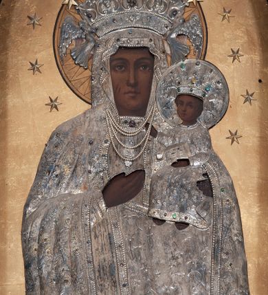 Zdjęcie nr 1: Obraz w formie stojącego prostokąta zamkniętego łukiem pełnym z przedstawieniem Matki Boskiej w typie Częstochowskiej. Maria została ukazana frontalnie, w półpostaci. Patrzy na widza, twarz ma owalną, o wyrazistych rysach, ciemnej karnacji, długim nosie, ciemnych oczach i niewielkich ustach. Prawą ręka wskazuje na trzymane na lewej ręce Dzieciątko Jezus zwrócone w trzech czwartych w prawo, z głową odwróconą do widza. Twarz ma okrągłą, o ciemnej karnacji i wyrazistych rysach, na prawym policzku dwa nacięcia. Włosy brązowe, kręcone, zaczesane na twarz. Lewą rączką podtrzymuje księgę, prawą ma uniesioną w geście błogosławieństwa. Ubrania postaci oraz nimby i korony wykonane są ze srebrnej blachy, trybowanej w ornament roślinny, podkreślonej perełkowaniem na krawędziach i kameryzowanej w partii lamowań oraz koron. Maria ma pod szyją zawieszone sznury pereł. Nimb Dzieciątka jest wykonany z blachy, Marii złocony, oba promieniste. Obie postacie mają otwarte korony przytrzymywane przez niewielkie anioły; koronę Marii dekoruje dodatkowo pięć płaskorzeźbionych, złoconych gwiazd. Wokół głów obu postaci 12 gwiazd, tło jednolite – złote. 